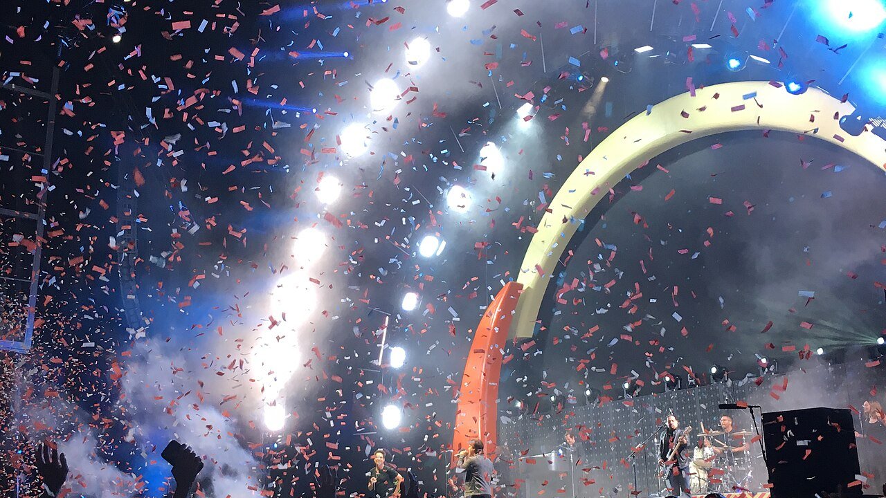 A festival crowd with raised hands as confetti falls in front of a lit stage
